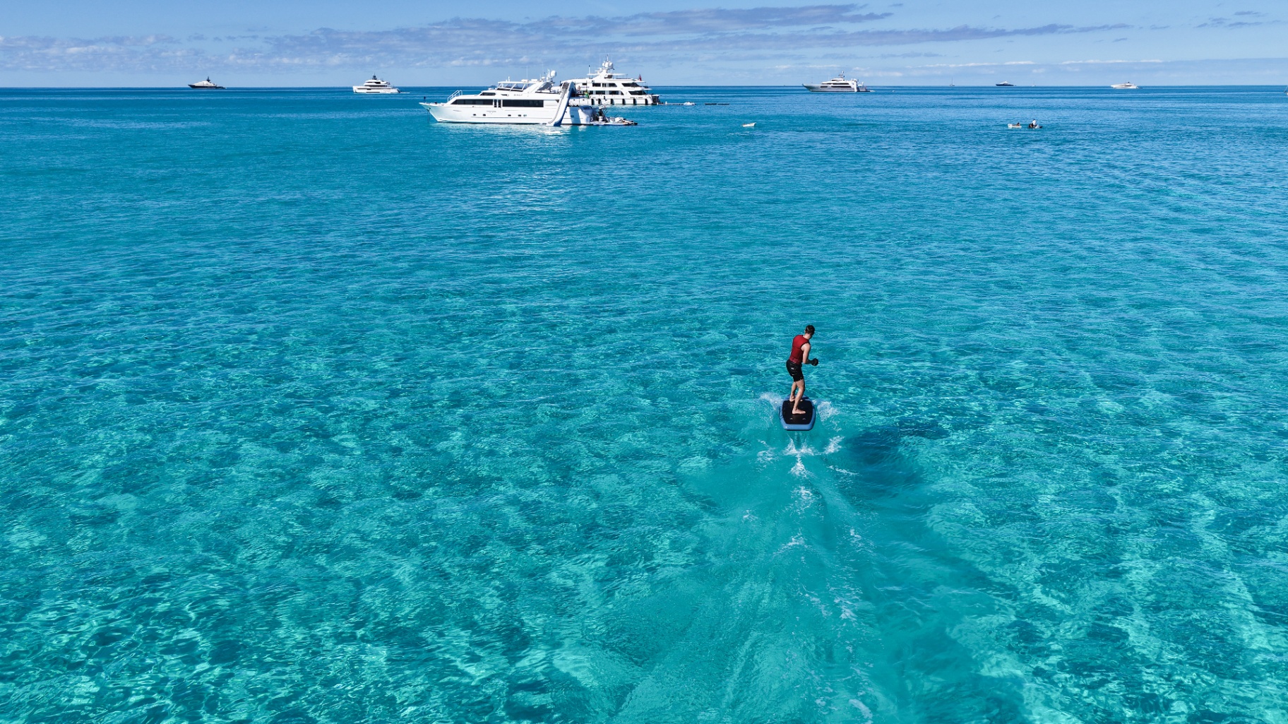 Guest riding an eFoil over clear turquoise water with Birdy anchored in the distance