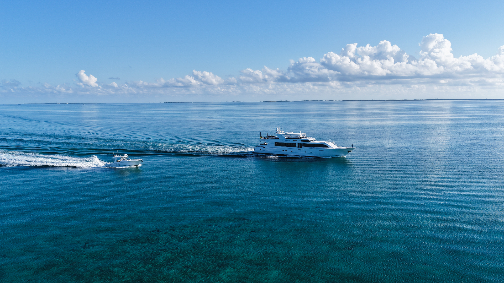Birdy cruising across calm blue water with a tender nearby