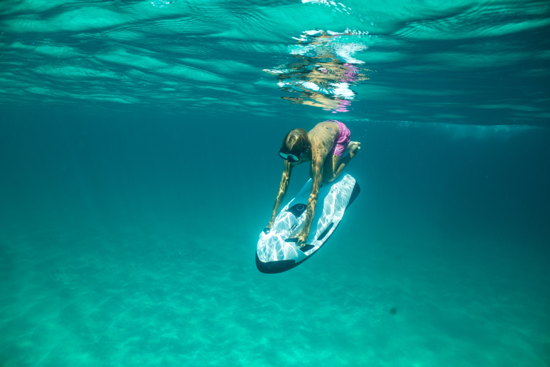 Guest riding a Seabob underwater scooter over a sandy bottom