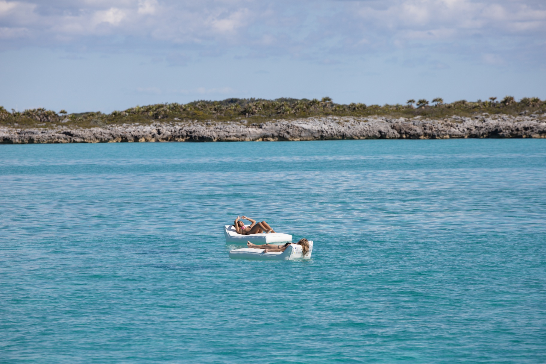 Two guests drifting on floating loungers off a deserted shore