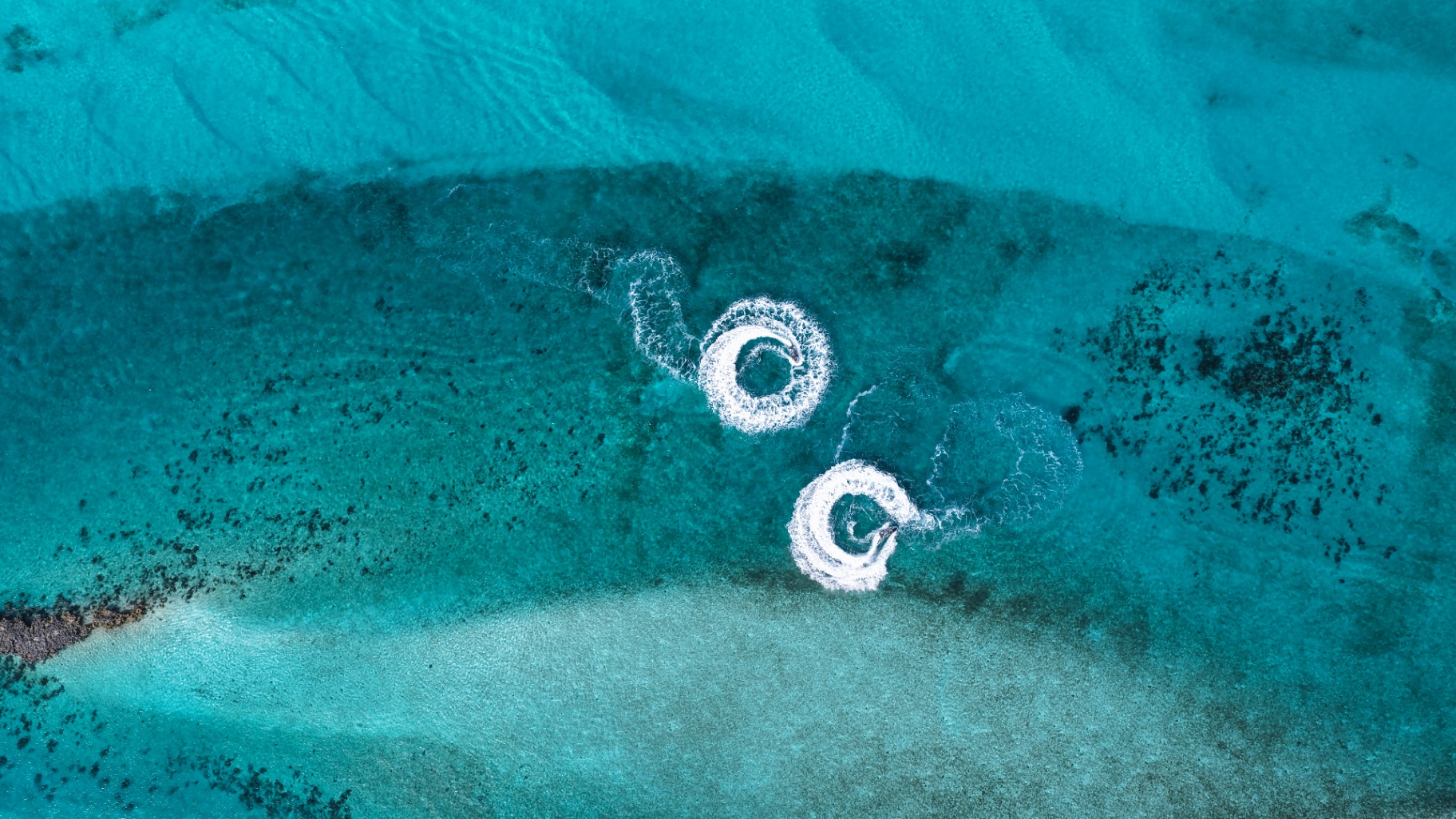 Two jet skis carving circles over a turquoise sandbar